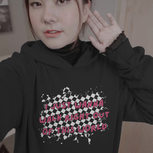woman wearing a black hoodie with rugged checkers and pink text "i just wanna walk right out of this world" in the front and a checkered road winding away, with text "goodby" on the back