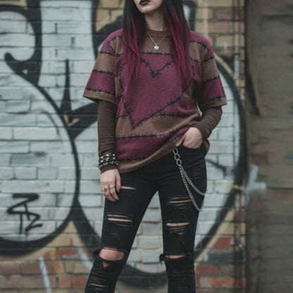 An alt style girl in a street setting wearing a knitted tee with dark barbed burgundy-brown stripes and a large barbed heart, worn over a long sleeve