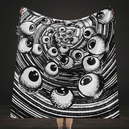 A large sherpa blanket with a black and white drawn vortex and eyeballs floating into it 