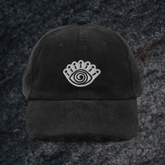 A black corduroy cap with an embroidered spiral eye symbol