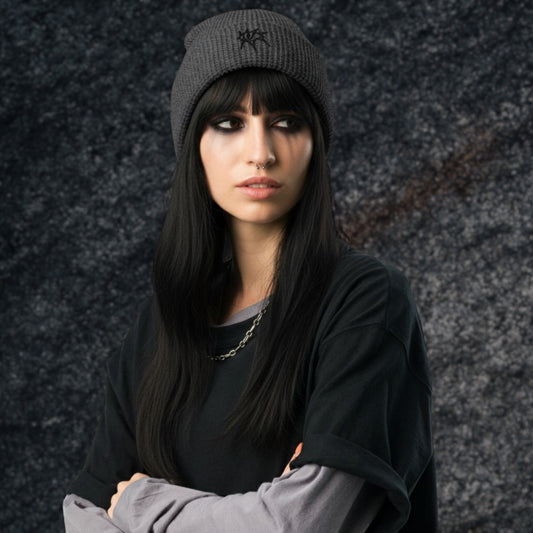 Alt style woman wearing a tee over a long sleeve and a waffle knit beanie with an emo grunge eye embroidery