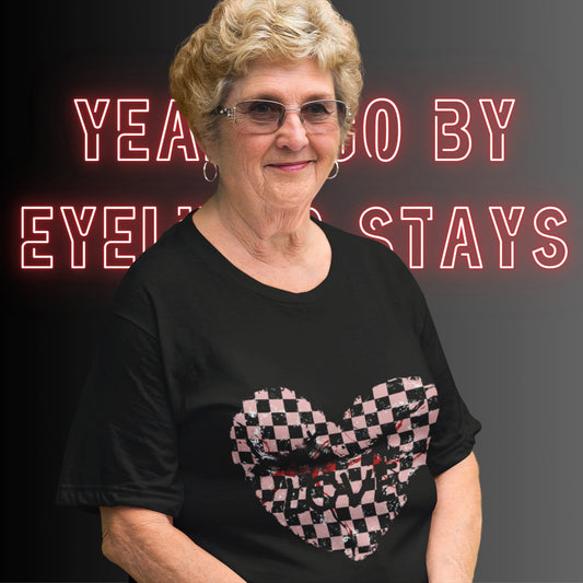 elderly emo woman wearing a black t-shirt with a pink and black cracked checkered heart and the text love partly obscured