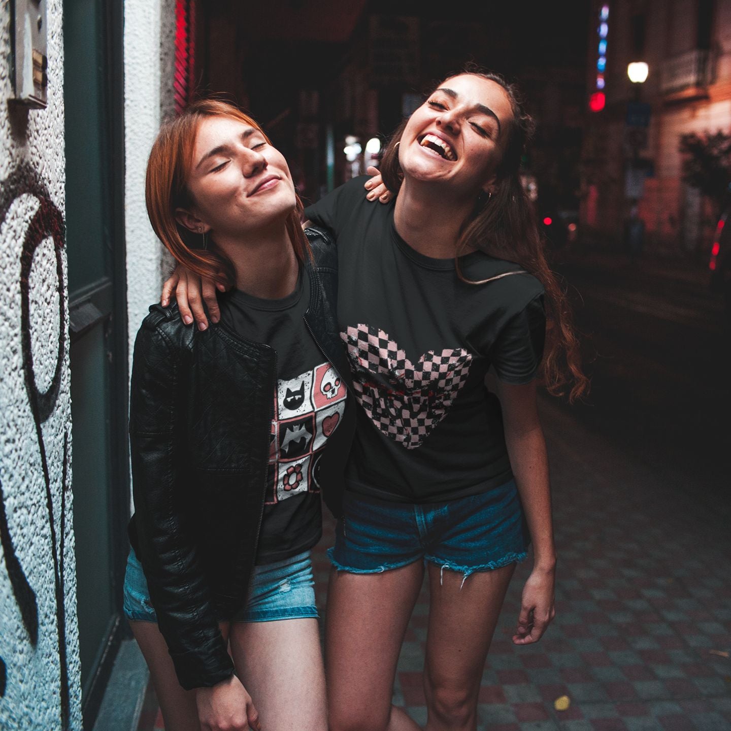 two women with black graphic alt t-shirts, one with an emo style cracked checkered heart