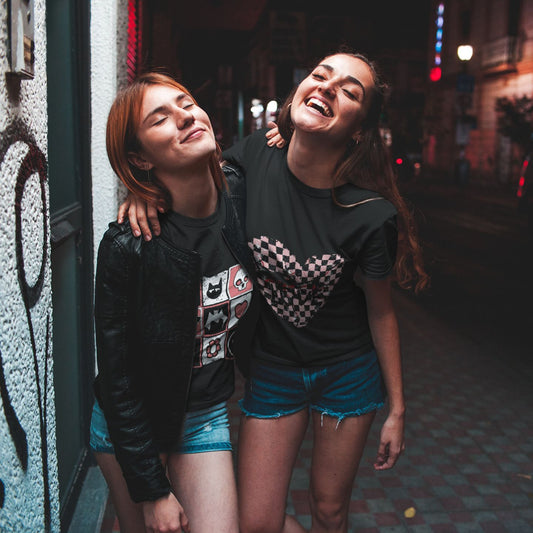 two women with black graphic alt t-shirts, one with an emo style cracked checkered heart
